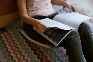 dama sentado en habitación con de colores alfombra, disfrutando su favorito nuevo revista acerca de arte, rollos mediante paginas foto