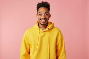 Overjoyed young pretty bearded man with dark skinned wearing sporty clothes while standing over pink background, keeping hands along body, looking at camera with wide happy smile photo