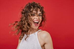 Joyful attractive blue-eyed lady in white top standing over red background, whirling and smiling happily with broad smile, showing her pleasant emotions with wide mouth opened photo
