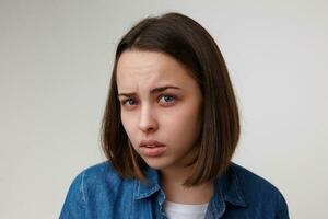 Close-up of young attractive short haired blue-eyed brunette lady squinting her eyes while looking wonderingly at camera, isolated over white background photo