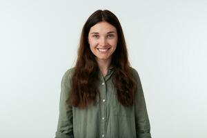 Cheerful young beautiful long haired brunette female showing her white perfect teeth while smiling happily, dressed in casual clothes while posing over white background photo