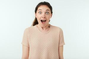 Studio photo of young attractive dark haired lady with ponytail hairstyle keeping her mouth wide opened while rejoicing about something, isolated over white background