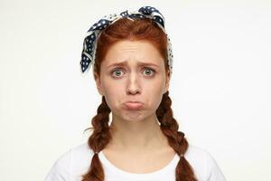 Indoor portrait of young ginger female posing over white background starring into camera with sad, depressed facial expression photo