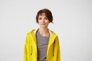 Portrait of positive young nice lady in yellow rain coat, enjoy the life, looks at the camera with happy expressions, smiling over white background. photo