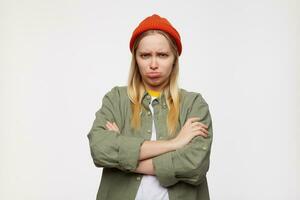 Offended young pretty white-headed female pursing sadly her lips and crossing hands on her chest, dressed in casual wear while standing over blue background photo