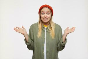 Indoor photo of young long haired white-headed lady shrugging confusedly with raised palms and grimacing her face, standing over blue background in casual wear