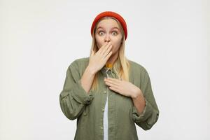 Amazed young attractive long haired blonde lady covering her mouth with raised palm and looking amazedly at camera with wide eyes opened, isolated over blue background photo