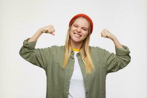 Cheerful young lovely long haired blonde woman with natural makeup raising joyfully her hands and squinting her eyes, isolated against blue background photo