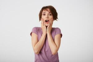 Portrait of happy amazed young attractive girl in with a surprised expression on her face, standing over white wall with wide open moth and eyed. Positive emotion concept. photo