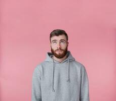 Portrait of young handsome guy looking up at the copy space and thinking about solving a problem, presents possible options, stands over pink background. photo