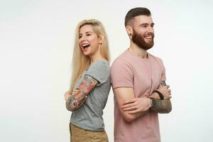 Horizontal shot of young joyful couple in casual t-shirts keeping hands crossed and looking ahead with wide happy smiles, standing over white background photo