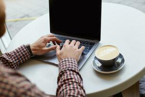 Men's hands are working on the keyboard of the laptop, nearly a gray cup of coffee on a white table. photo