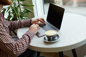 Clouse up of men's hands are working on the keyboard of the laptop on a white table, nearly a gray cup of coffee. photo