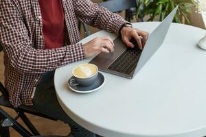 Clouse up in a cafe on a white table, men's hands are working on the keyboard of the laptop, next to a gray cup of coffee. photo