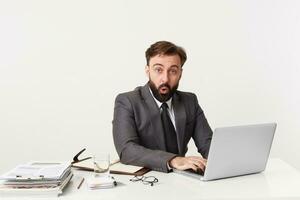 Portrait up of dressed in a suit respectable office worker sitting at desktop looking straight in confusion disbelief, mouth opened from shocking news. photo