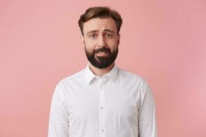 Portrait of a handsome bearded man who is regretful that has just destroyed a house of cards. Frown and looking at camera isolated pink background. photo