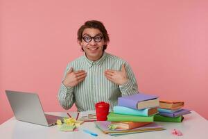 Portrait of cheerful young man with dark hair looking at camera happily and raising eyebrows surprisedly, pointing to himself with raised palms, isolated posing over pink background photo