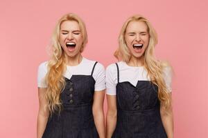 Stressed young pretty white-headed women with loose hair frowning their faces with closed eyes while screaming excitedly, isolated over pink background photo