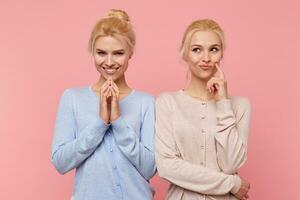 Beautiful young blonde twins conceived something interesting and do not want to disclose their secret to anyone. Look mysterious and thoughtful isolated over pink background. photo