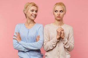 Young blonde lady mockingly looks at his sister isolated over pink background, who was frightened spider. photo