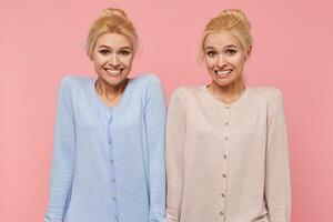 Beautiful young blonde twins confused and unable to explain and understand the current situation, shrug and smile isolated over pink background. photo