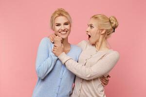 Photos of twins, hug each other and hold hands, one sister is surprised at the second one, who smiles broadly and looks into the camera, stads over pink background.