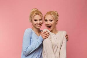 Photo of cute twins blondes, posing for a family album and photos to send them to grandma. Having fun and smiling widely into the camera, stands over pink background.