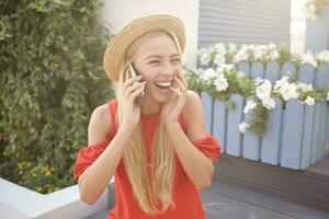 Bright photo of young lovely white-headed woman in elegant clothes laughing happily while talking to her friend on phone, posing outdoor on warm summer day