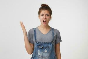 The young girl in amazement is displeased, cannot understand how this happened, is indignant, angry, her hand is raised up. Portrait of annoyed screaming woman, isolated over white background photo