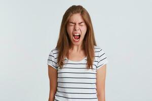 Closeup of crazy hysterical young woman with eyes closed and opened mouth wears striped t shirt feels angry and screaming isolated over white background photo