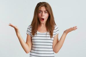 Closeup of mad irritated young woman with opened mouth wears striped t shirt shouting and holding copy space at both palms isolated over white background photo