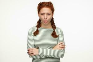 Indoor portrait of young ginger female standing over white background showing her tongue with angry facial expression photo