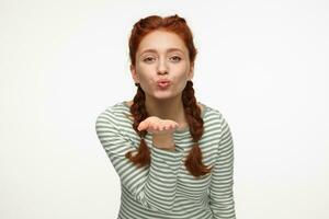 portrait of young ginger female standing over white studio background sending air kiss into camera photo