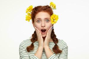 Indoor portrait of young ginger female posing over white background starring into camera with shocked facial expression photo