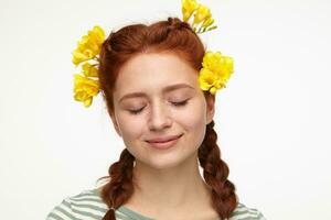 Indoor portrait of young ginger female posing over white background keeps her eyes closed with tender smile on her face photo