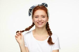 portrait of young ginger female standing over white studio background smiles and touching her hair photo