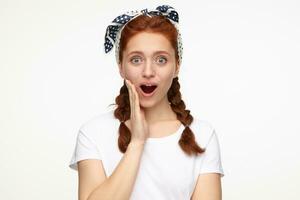 portrait of young ginger female standing over white studio background starring into camera with shocked facial expression photo