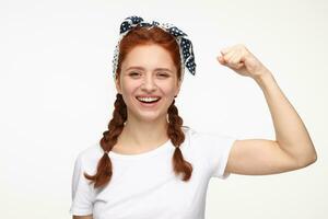 portrait of young ginger female standing over white studio background smiles and shows her muscles photo