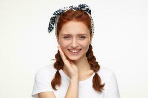 portrait of young ginger female standing over white studio background smiles broadly and looks directly into camera photo