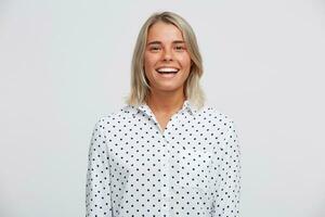 Portrait of cheerful beautiful blonde young woman wears polka dot shirt feels happy, standing and smiling isolated over white background photo