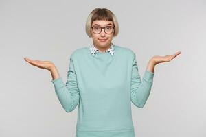 Portrait of confused pretty young woman wears blue sweatshirt and glasses feels embarrassed and holding copyspace at both palms isolated over white background photo