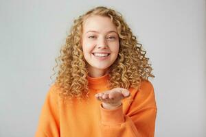 Romantic gestuers. Beautiful young curly blonde girl sending air kisses with charming smile. Studio shot on white background. photo