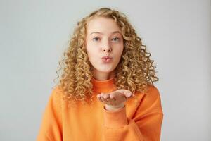 Blowing sending air kiss lovely pretty curly girl with pout lips isolated on white background, shows tender feelings.Sweet kiss directly to the camera. photo