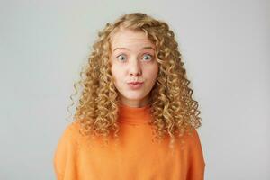 Headshot of pretty curly blonde girl staring in camera with popped eyes isolated on white background, looks with misunderstanding, carelessly, naive. photo