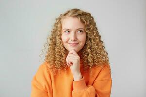 Cleverly smiles thoughtful blonde thinking about her boyfriend, looks rightside, makes plans, holds her fist near her chin, isolated over white background photo