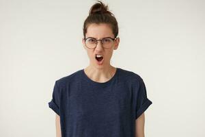 Angry, irate woman in glasses with grumpy grimace on her face,with mouth opened in shout, ready to argue and swear, wants to gain respect, show strength, isolated over white background photo