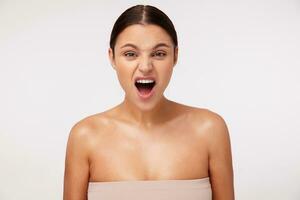 Indignant young attractive dark haired female with casual hairstyle frowning her face and keeping mouth opened while looking excitedly at camera, isolated over white background photo