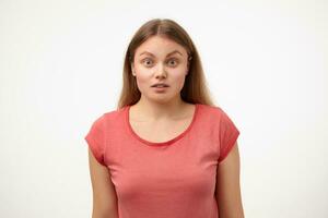 Portrait of bemused young blonde female rounding amazedly eyes while looking surprisedly at camera, keeping hands down while posing over white background photo