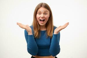 Agitated young pretty long haired woman with casual hairstyle raising emotionally palms while looking surprisedly at camera with wide mouth opened, isolated over white background photo