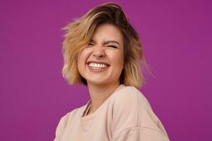 Indoor portrait of young dyed blonde female, with tattooed arms smiles broadly and keeps her eyes closed, isolated over purple background photo